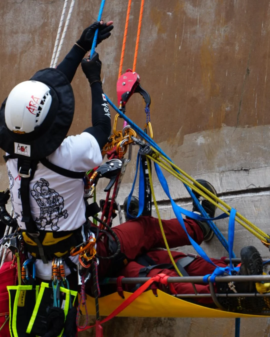 A rescuer working a litter on a rope face, with a red descender on the line above
